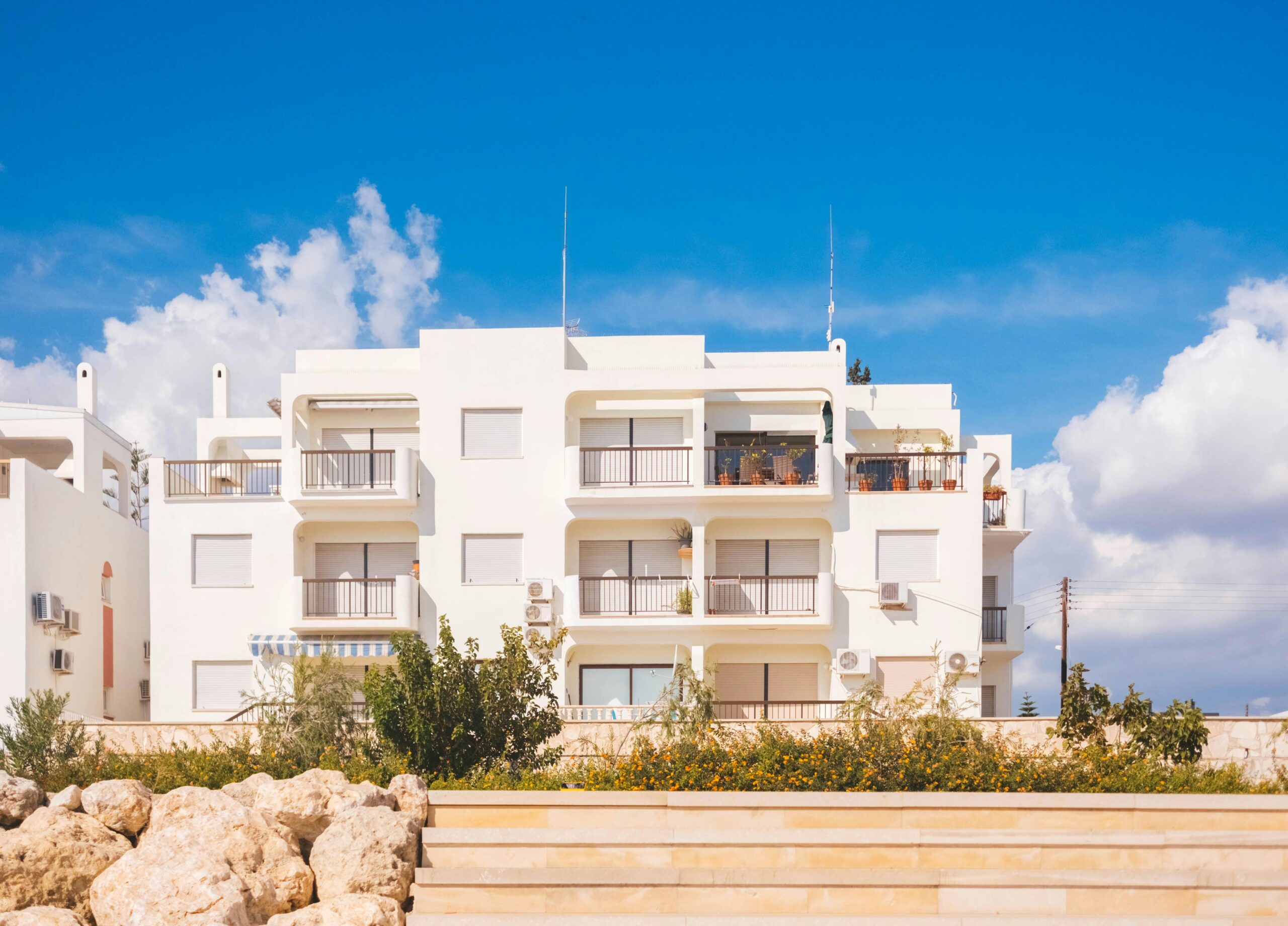 Stylish white apartment building exterior with balconies under a vibrant blue sky, showcasing modern architectural design.