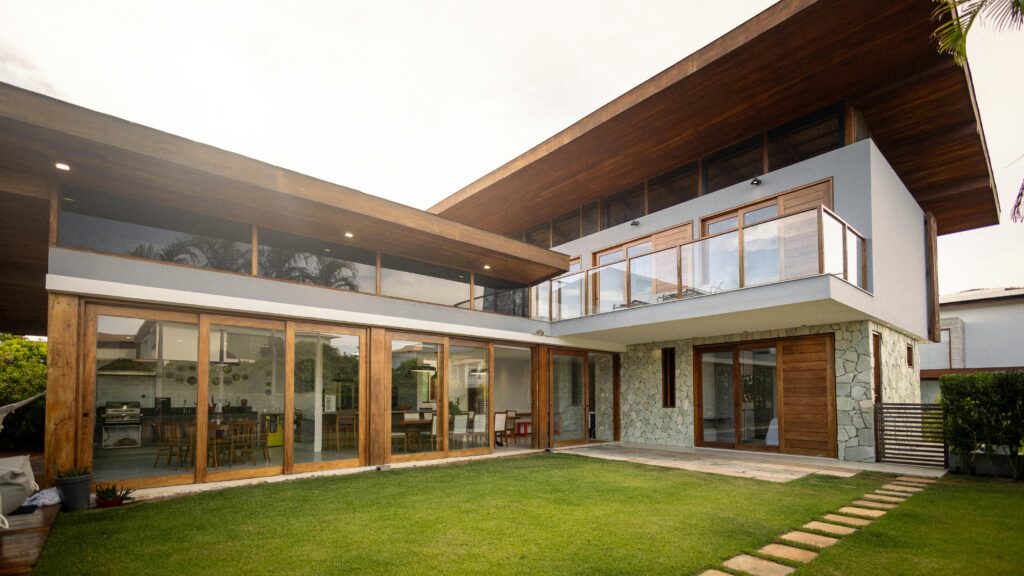 Contemporary luxury house exterior with large glass windows, wooden decor, and green lawn.